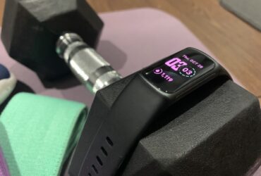 Fitbit Charge 5 draped over a dumbbell with other workout gear.