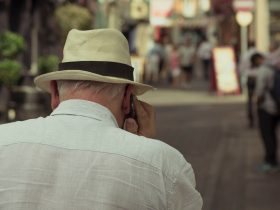 Elderly man walking down the street on a cell phone.