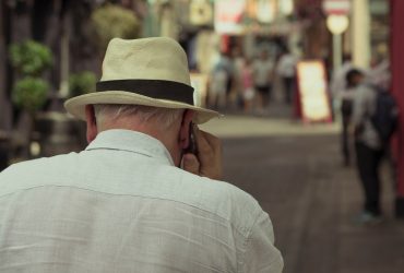 Elderly man walking down the street on a cell phone.