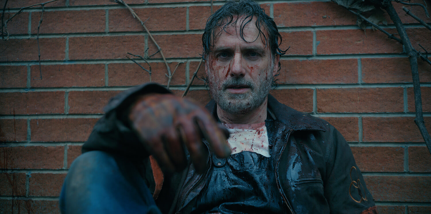 Rick Grimes in The Walking Dead: The Ones Who Live sitting on the ground, bloody and dirty.