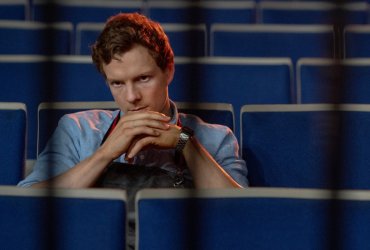 Dexter with his hands clasped at his chin in stadium seats in Dexter: Original Sin