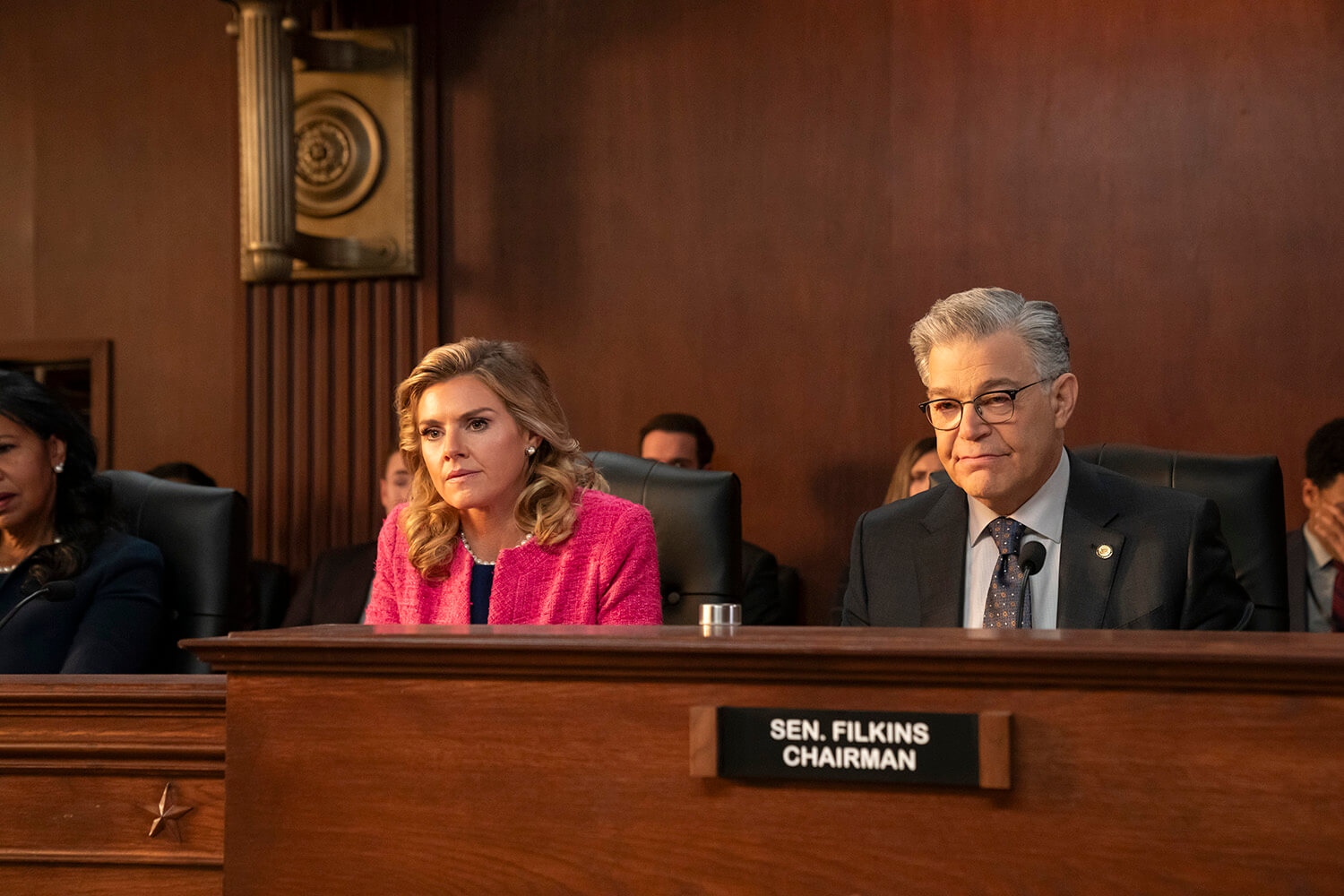 Two senators sitting behind a desk during a hearing in The Residence.