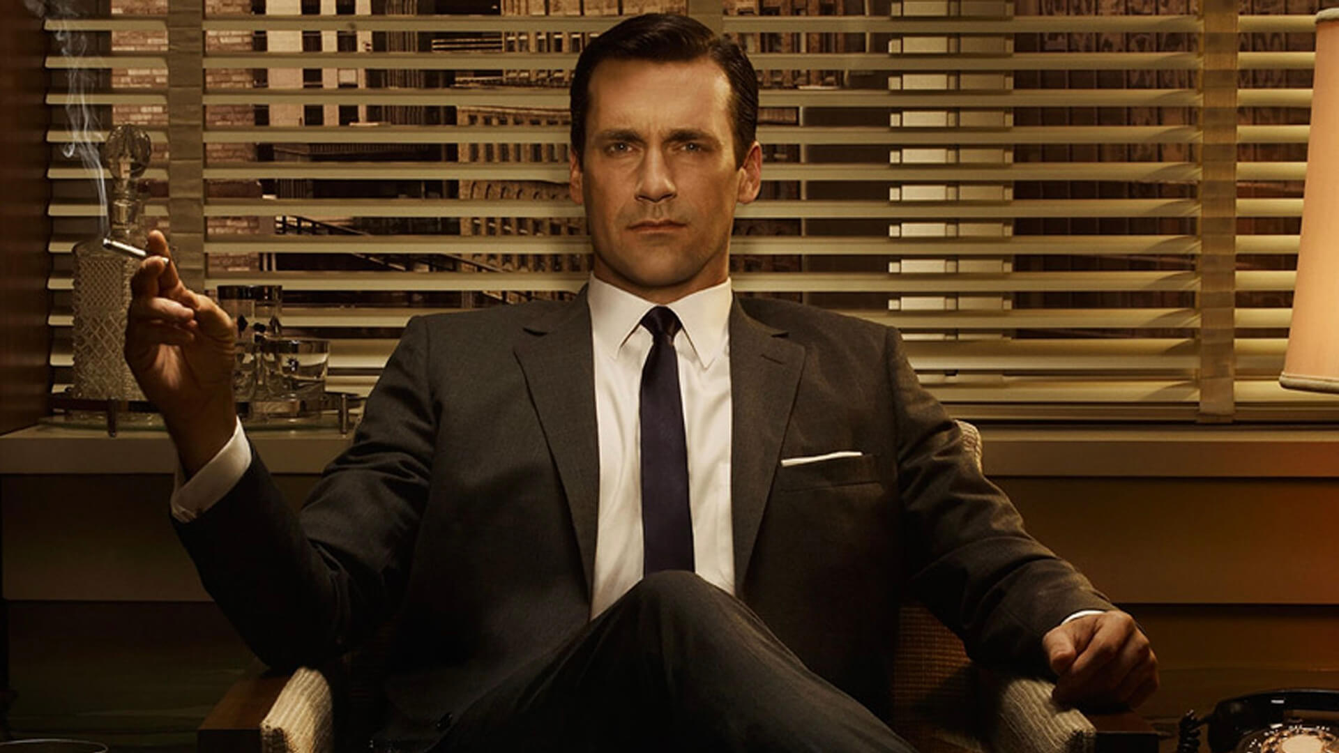 Don Draper in a suit sitting and smoking in Mad Men.