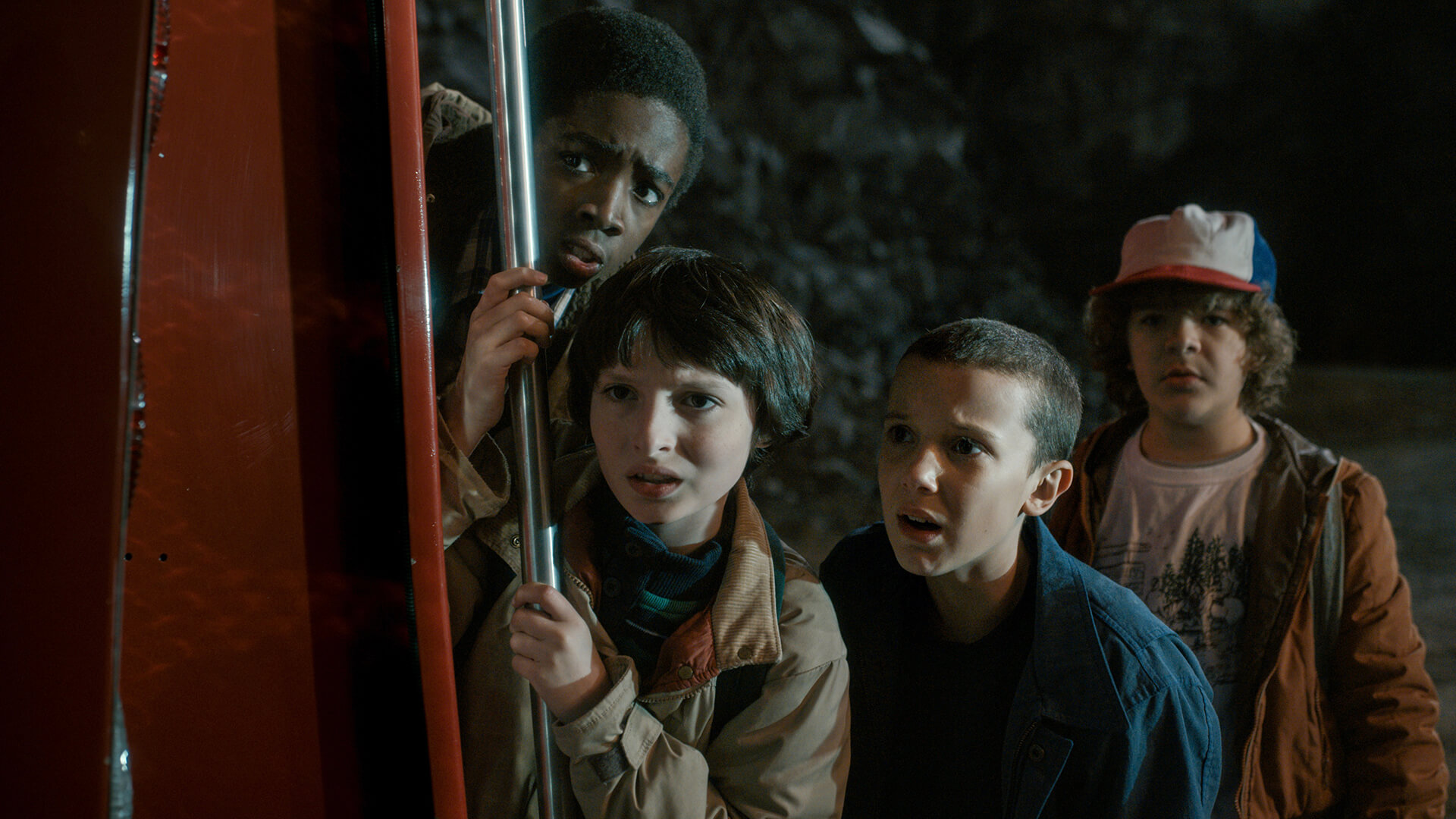 Four kids peak around a corner looking scared in Stranger Things.