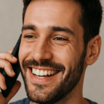 A man smiling while talking on a cell phone.