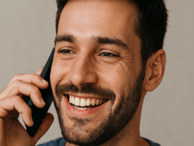 A man smiling while talking on a cell phone.