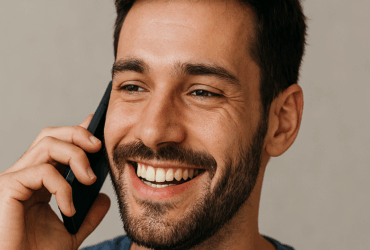A man smiling while talking on a cell phone.
