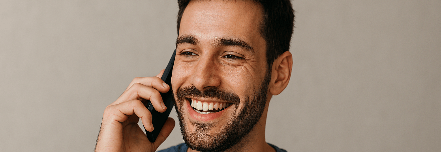 A man smiling while talking on a cell phone.