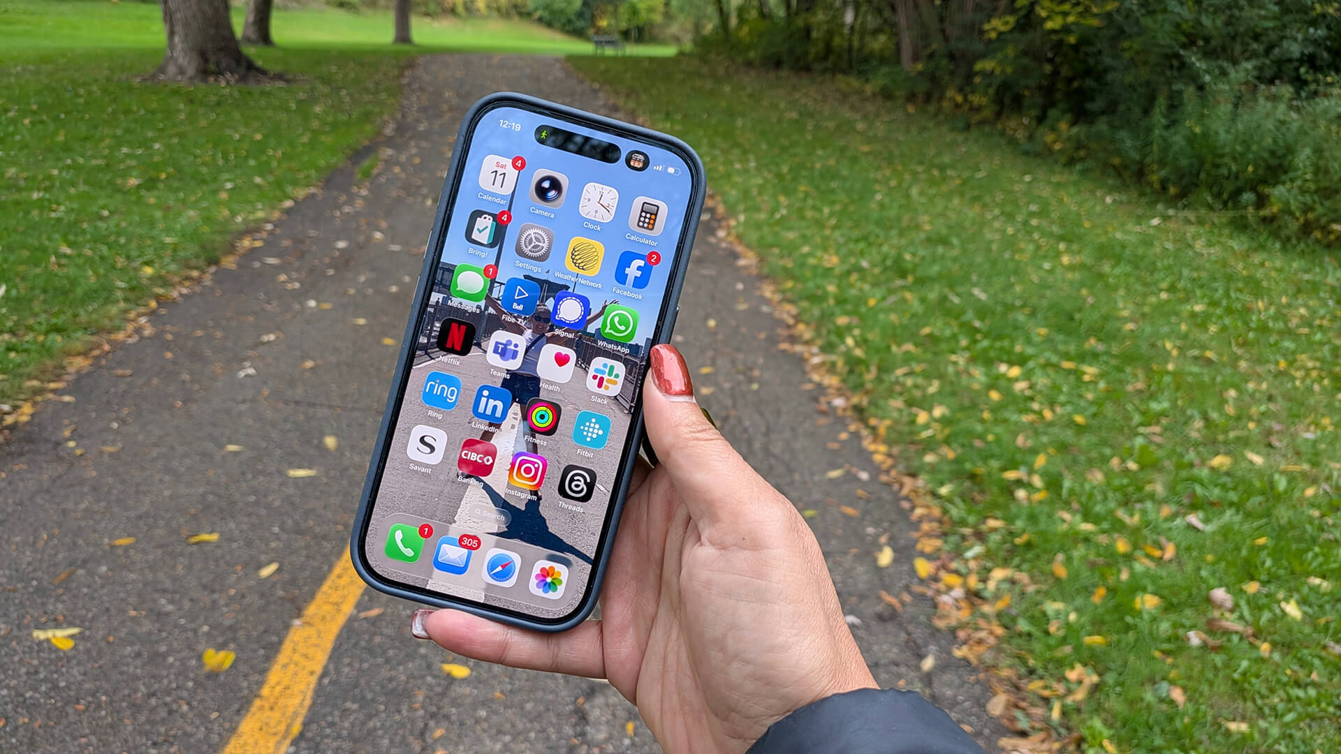 A hand holding an iPhone 17 Pro on a trail.