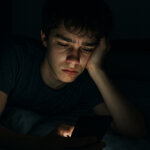 A young boy on his phone in the dark looking sad.
