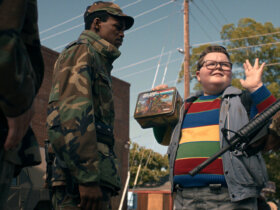 Derek with his hands up being approached by military men in Stranger Things.