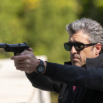Angelo wearing sunglasses outside pointing a gun in Memory of a Killer.