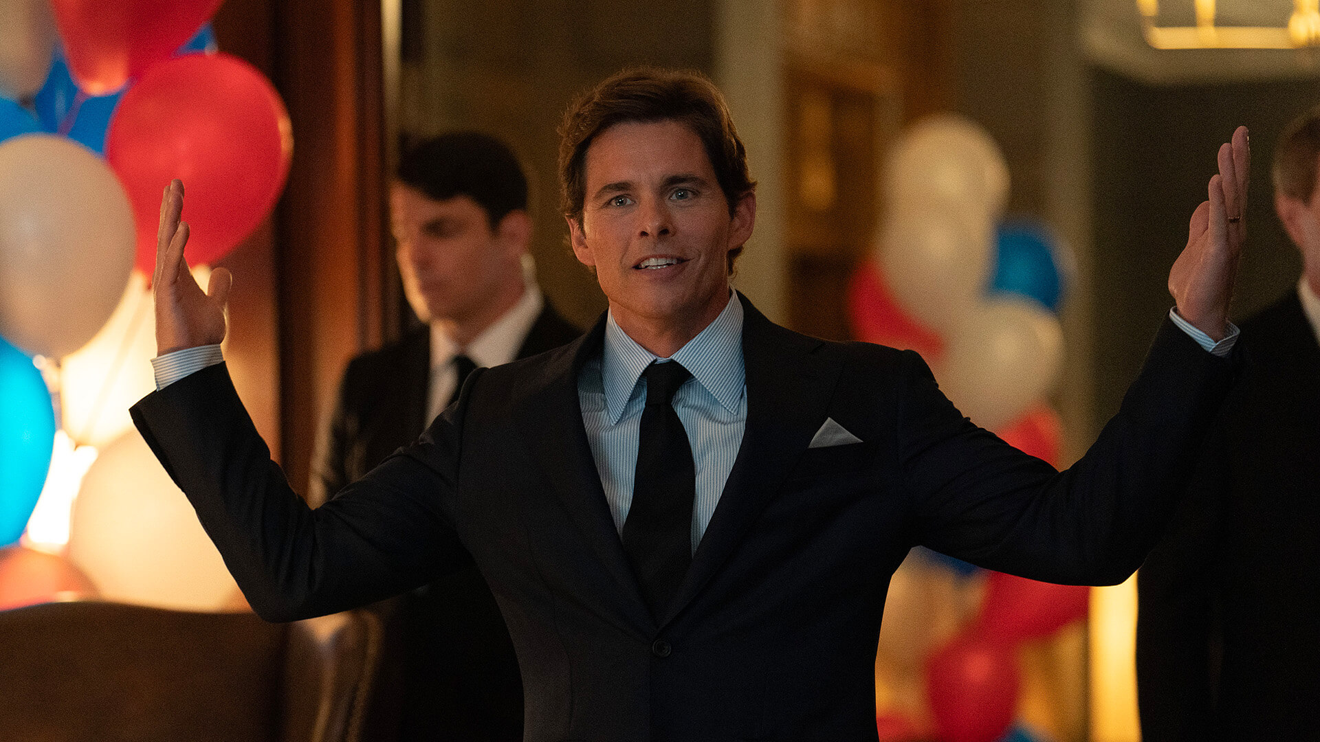 Cal standing in a suit at a party with his hands out in Paradise.
