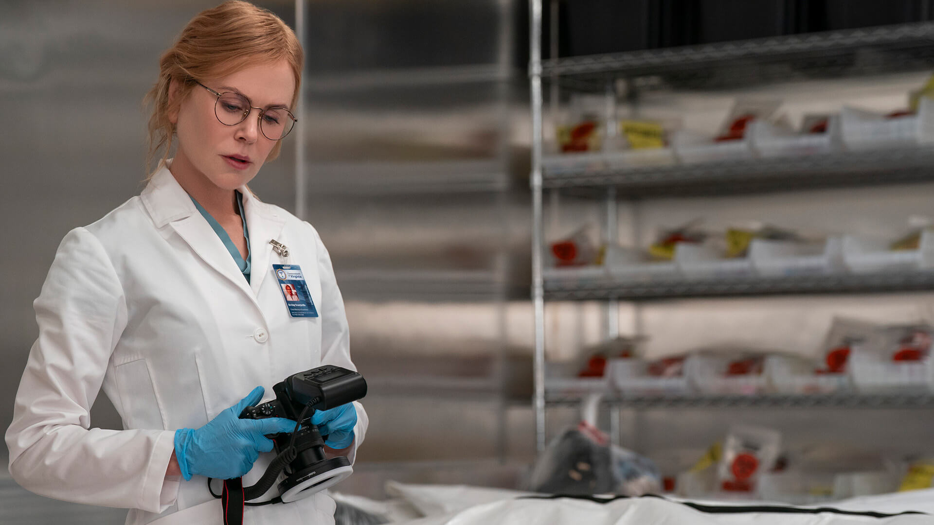 Kay in a white lab coat holding a camera in Scarpetta.
