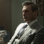 Coop in a suit in his office thinking in Your Friends & Neighbors.