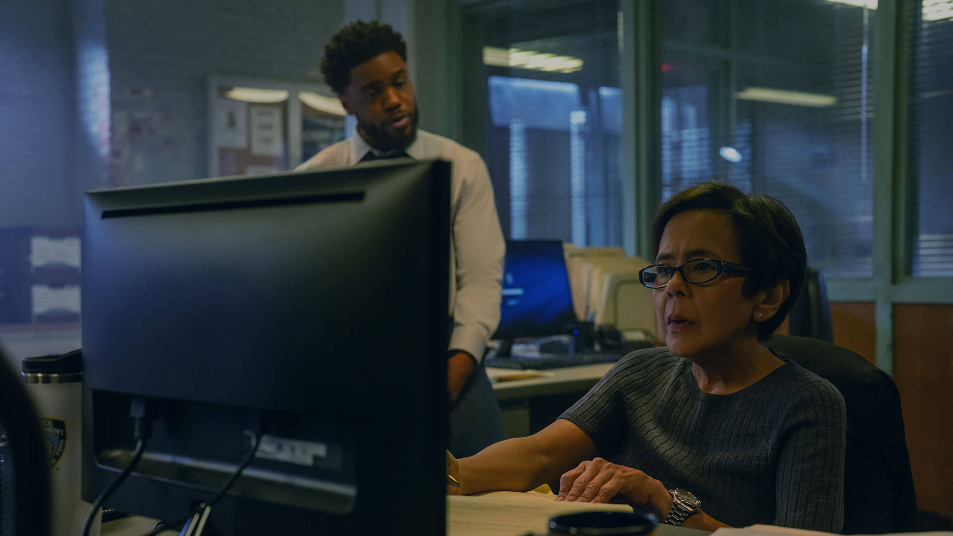 A detective at her computer as another looks on in Maximum Pleasure Guaranteed.