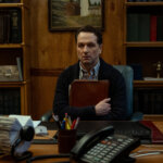 Tom sitting in his office clutching a folder in Widow's Bay.