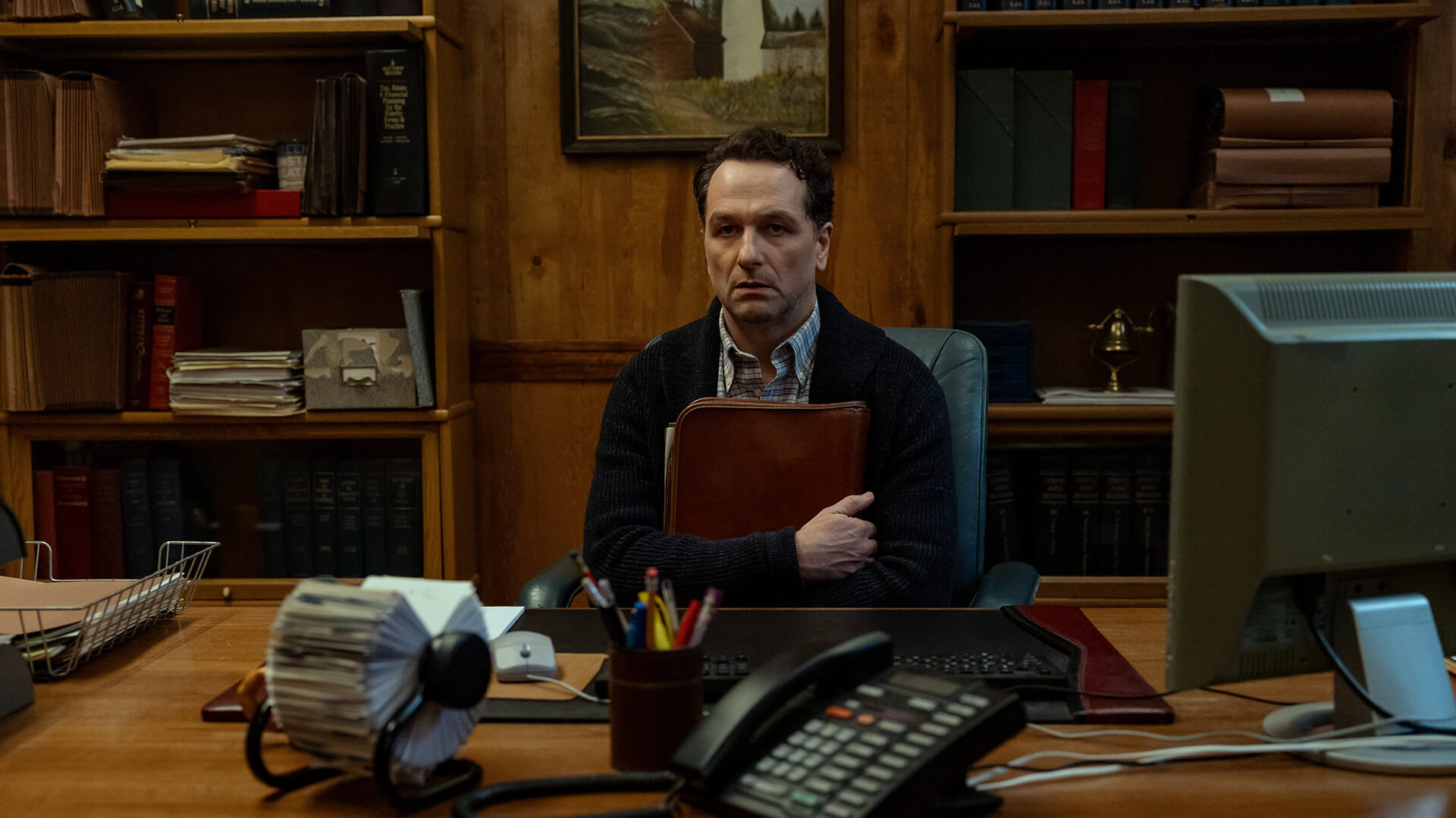 Tom sitting in his office clutching a folder in Widow's Bay.
