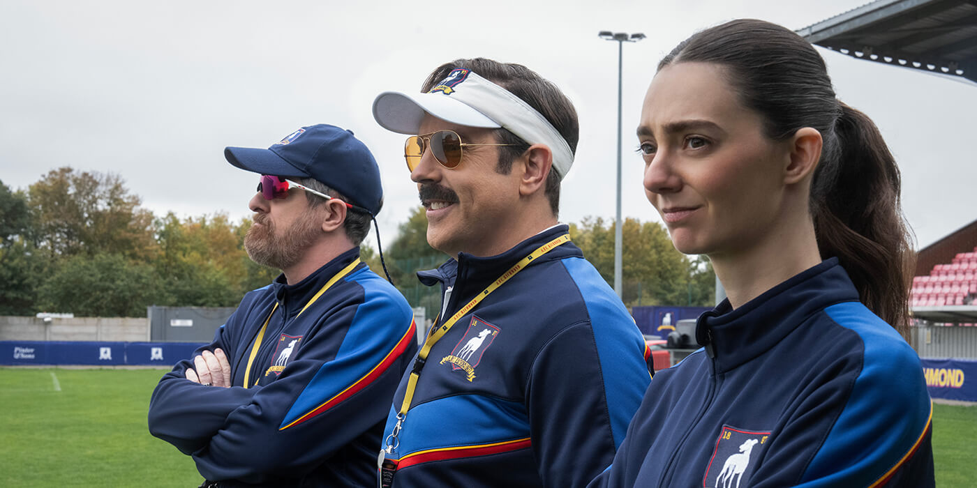 Coach Beard, Ted, and Alice standing in a line on the field in Ted Lasso.