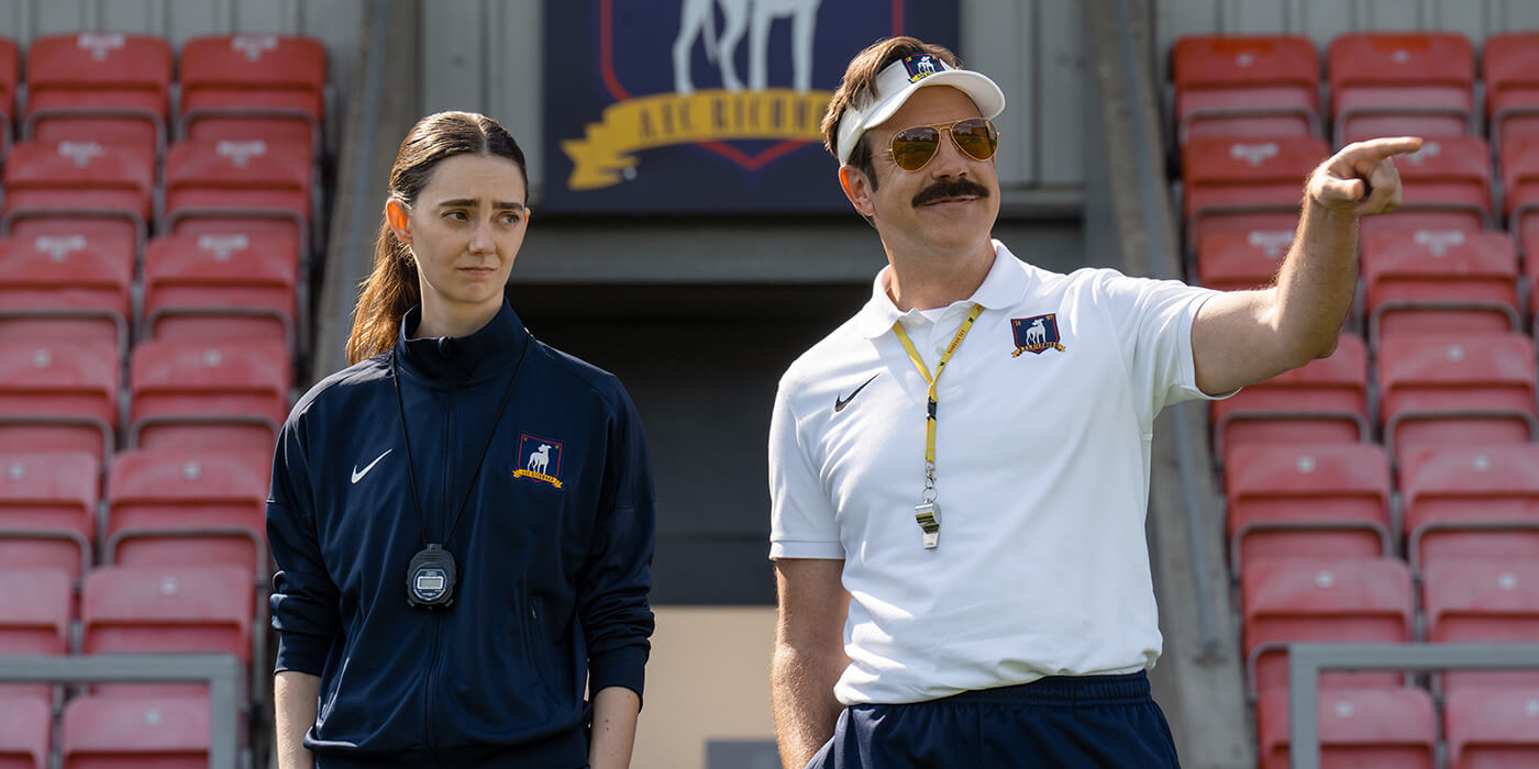 Ted and Alice standing on the sidelines coaching in Ted Lasso.