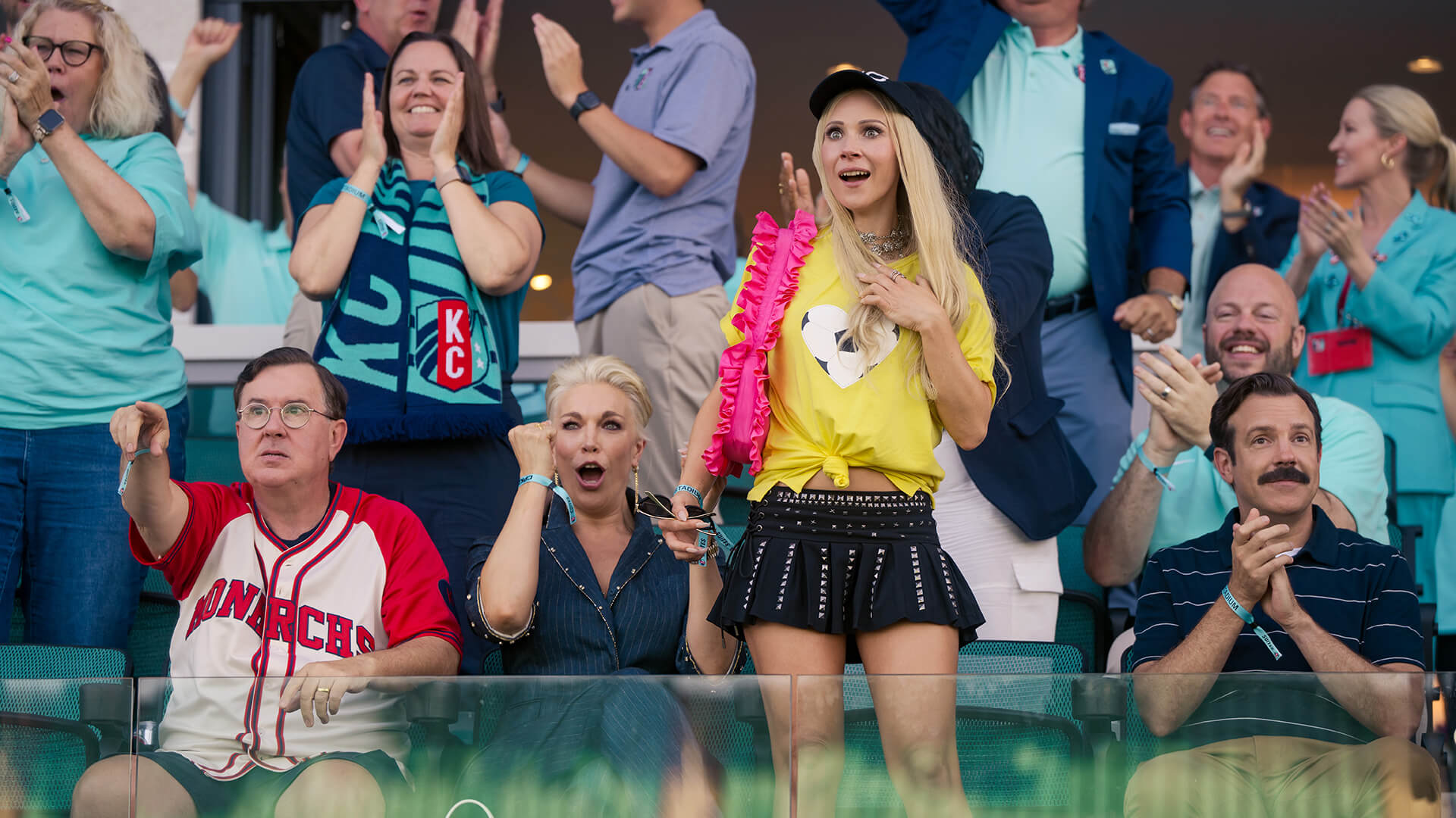 Keeley standing up in the stands cheering for the team in Ted Lasso.