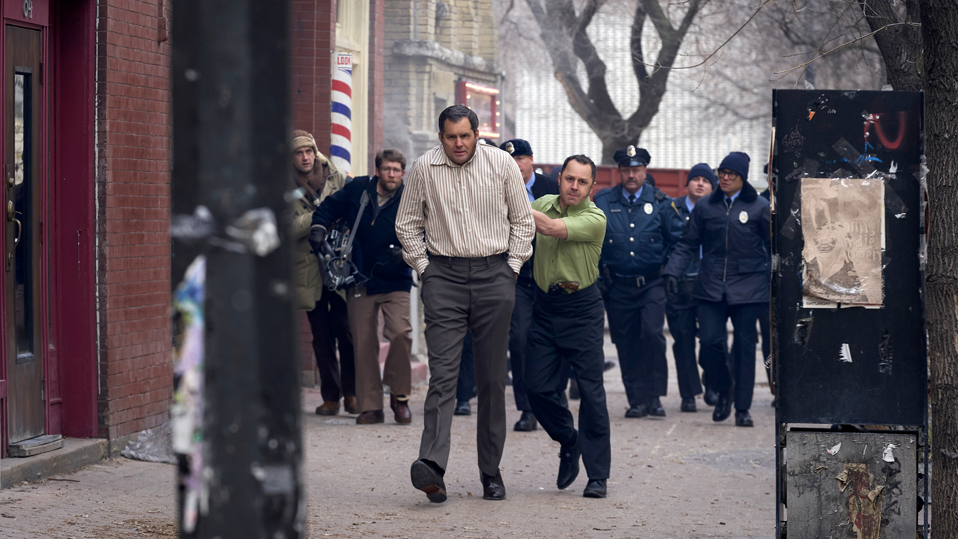 Tony walking Dick through the streets with a gun to his head and officers behind them in American Hostage.