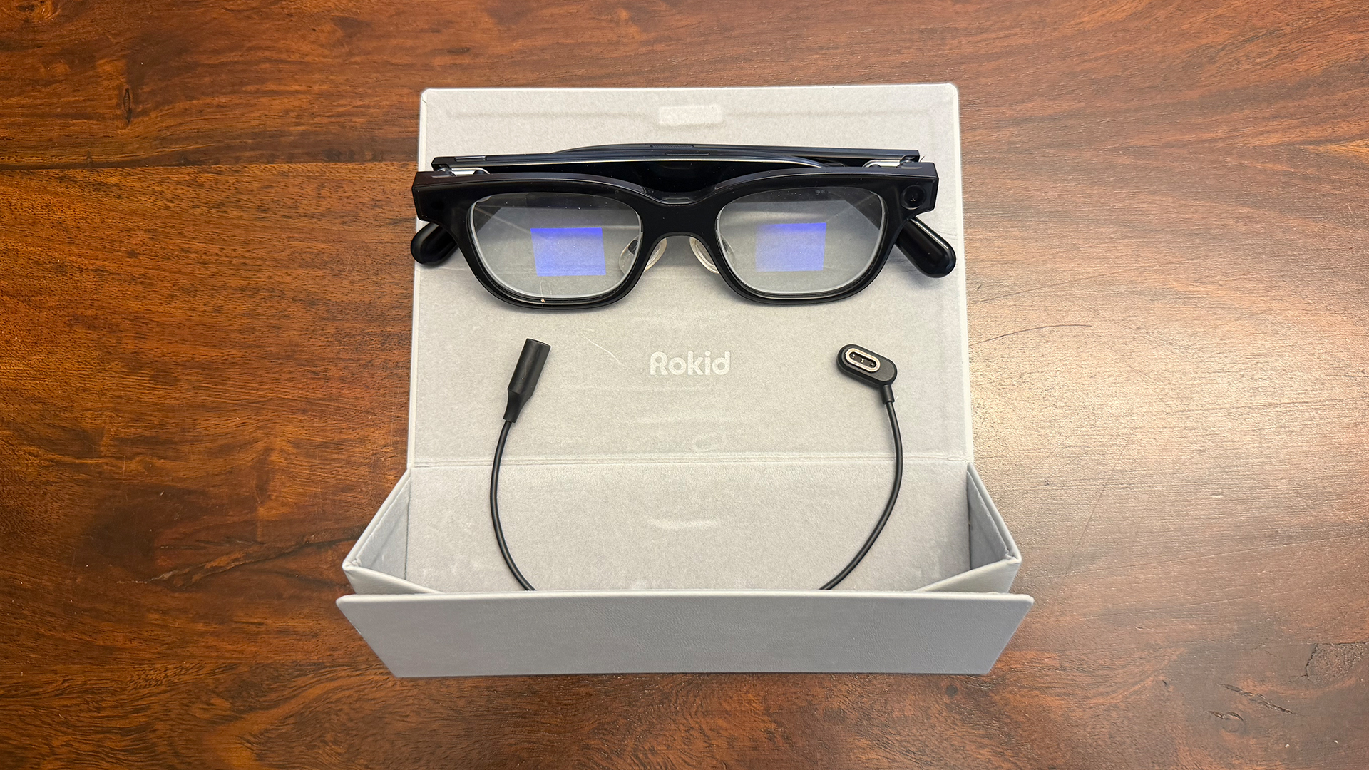 The Rokid smart glasses atop their case with the charging cable.