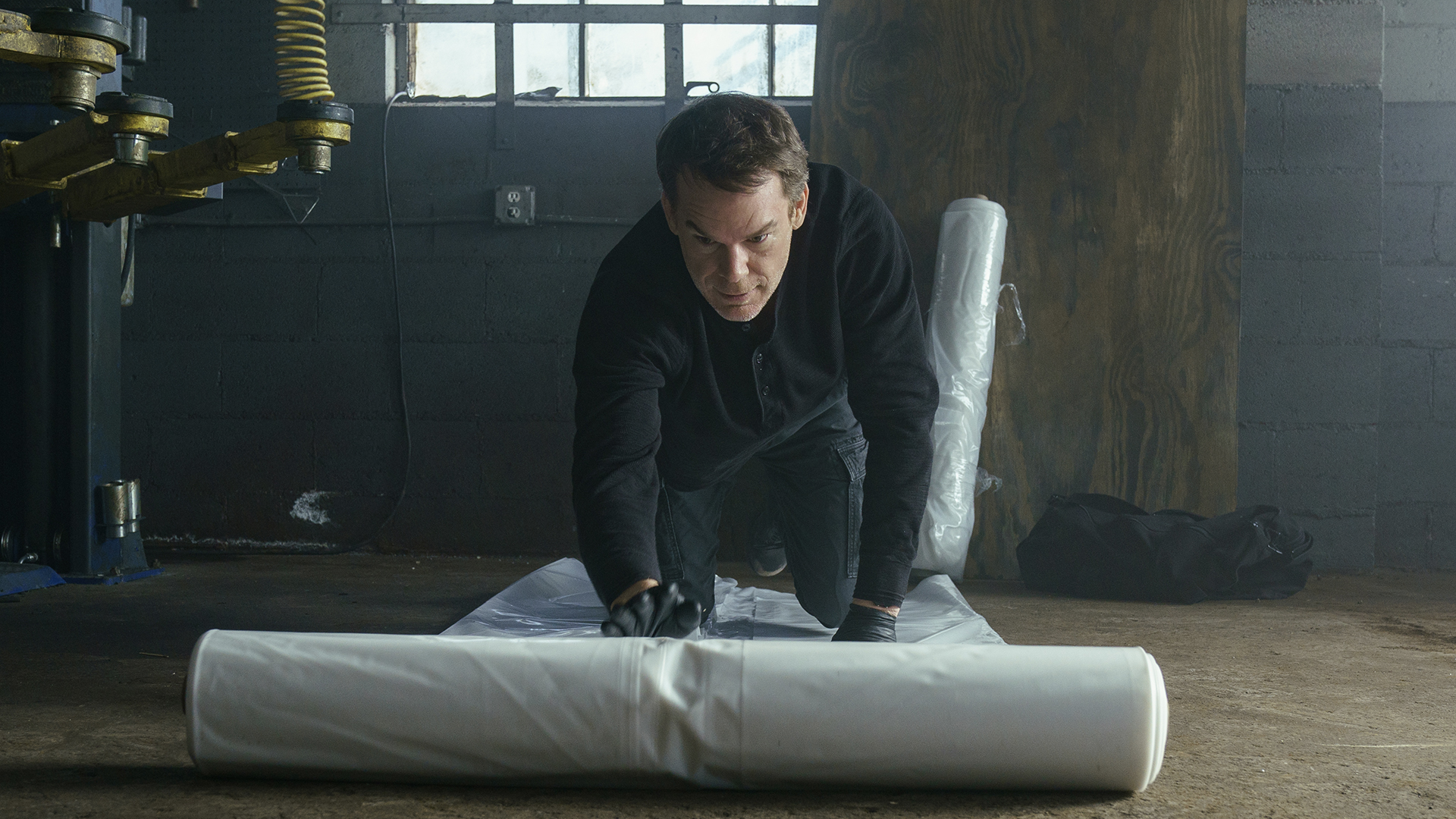 Dexter rolling out plastic on the floor of a warehouse in Dexter: Resurrection.