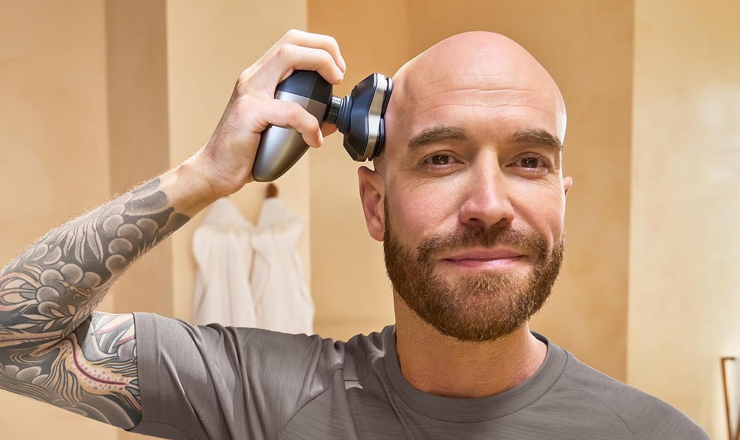 A man with tattoos shaving his bald head with the Philips Head Shaver Pro 9000.